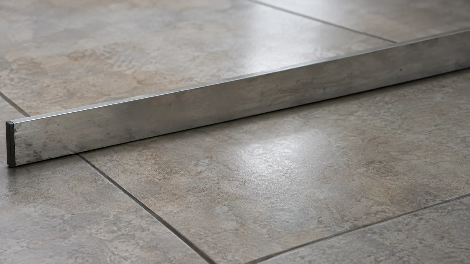 A close-up of a finished tile floor with a straight edge lying across the surface to check for lippage